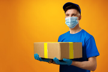 Young delivery man in face mask and gloves holding cardboard box parcel