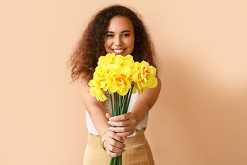 Beautiful young African-American woman with narcissus bouquet on color background