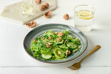 Plate with fresh salad and walnuts on light wooden background