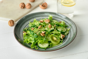 Plate with fresh salad and walnuts on light wooden background