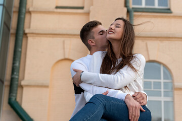 Happy young loving couple hugging in the background of urban architecture. Guy kissing his girlfriend