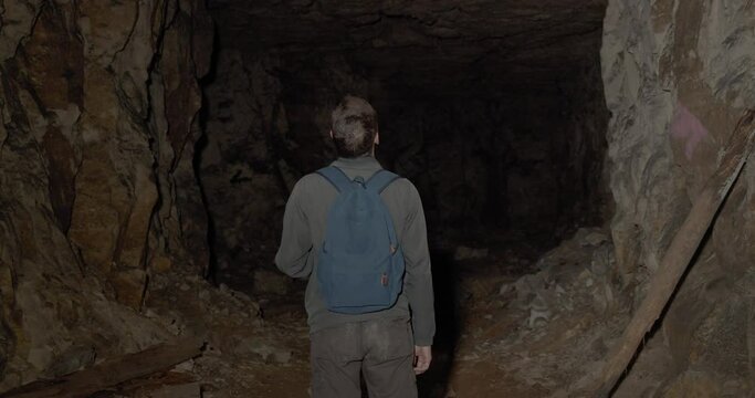 Traveler with a backpack in a dark cave with a flashlight. The man is at a dead end. No exit.