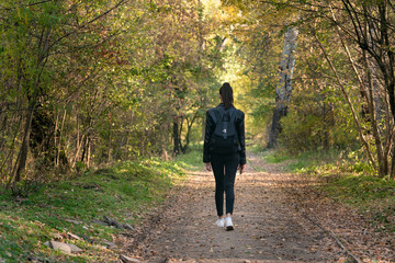 Young woman is walking along the alley of the park. Alone with myself. Back view.