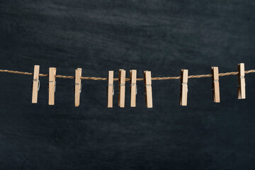 Fototapeta premium Several wooden cloth clips in rope waiting for clothes to come after laundry. Black wall on the background