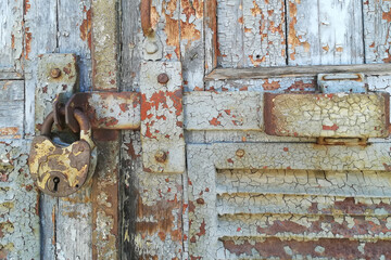 Weathered vintage wooden door peeling turquoise paint with rusty latch and heavy lock padlock.