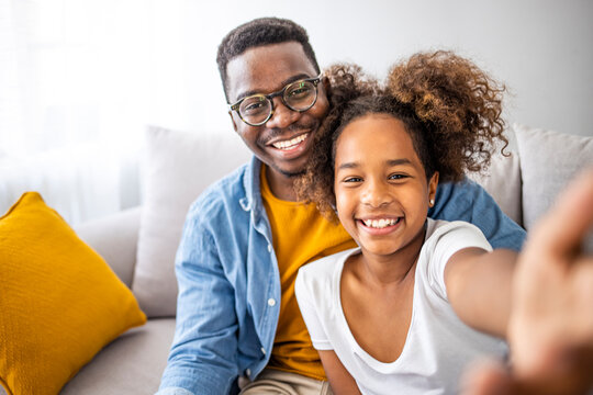 Family time. Happy father taking selfie with his cute daughter at home, sitting on sofa. Nice selfie! Self portrait of young father and his little daughter smiling