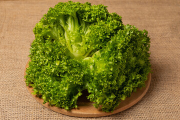 three bunches of lettuce lies on a round wooden board, against a background of linen fabric, close-up