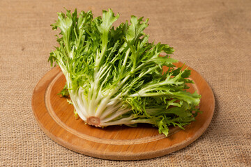 a bunch of frillis lettuce lies on a round wooden board, against a background of linen fabric, close-up