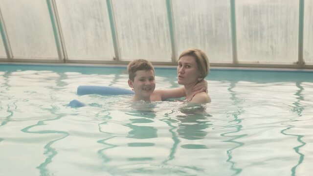 Mother teaching seven-year-old son or child to swim in the swimming pool.
