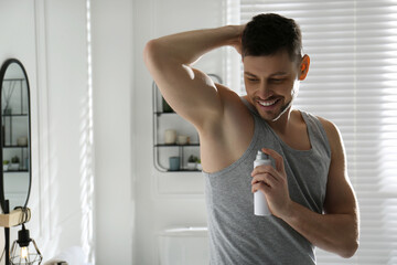 Handsome man applying deodorant in bathroom. Space for text - obrazy, fototapety, plakaty