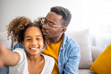 Fototapeta premium Smiling black father and child daughter taking selfie together looking at camera, head shot portrait of happy african family dad with kid embracing posing making photo recording video, phone cam view