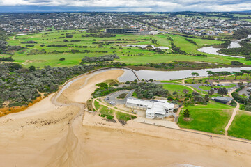 Aerial view of a river running through a golf course and over a beach past a surf lifesaving club