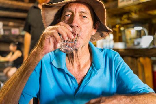 An elderly man raising a glass to his mouth in an outback pub