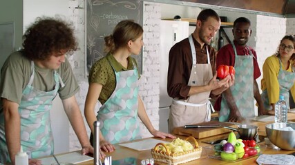 Male chef showing red bell peppers and speaking to group of young multiethnic men and women at cooking master class