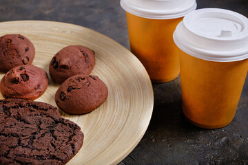 Two glasses takeaway coffee and an American cookie on dark background.