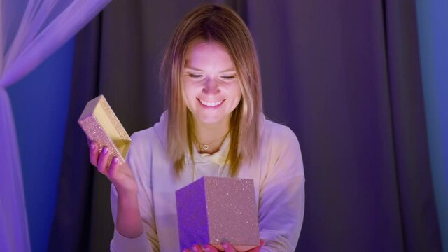 Beautiful blonde young woman opening surprise gift box with light inside. Caucasian female receiving Birthday, Christmas or New Year gift at magic night. Shot on RED Helium Weapon camera 8K footage