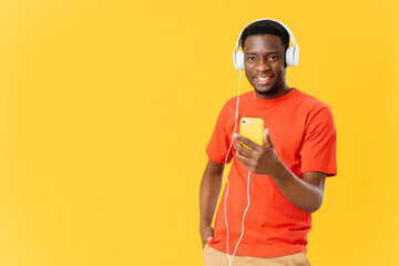 Cheerful African American with a phone in his hands in headphones listens to music yellow background fashion