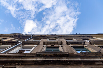 Fototapeta premium an old gray house facade with many windows in front of a blue sky with white clouds. in a rustic house wall is a monument in the shape of a head. 