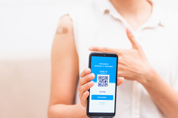Asian young woman pointing to adhesive plaster on arm her vaccinated and showing app smartphone mobile digital screen vaccinated coronavirus (COVID-19) certificate after getting vaccine prevent