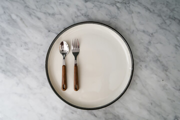 
Spoon and fork on an empty plate with empty space beside it on a marble table
