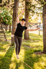 Slacklining is a practice in balance that typically uses nylon or polyester webbing. Girl walking on a slackline in a park during a sunset. Slack line