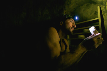 Side view of muscular farmer with headlamp checking homemade cheese in cellar 
