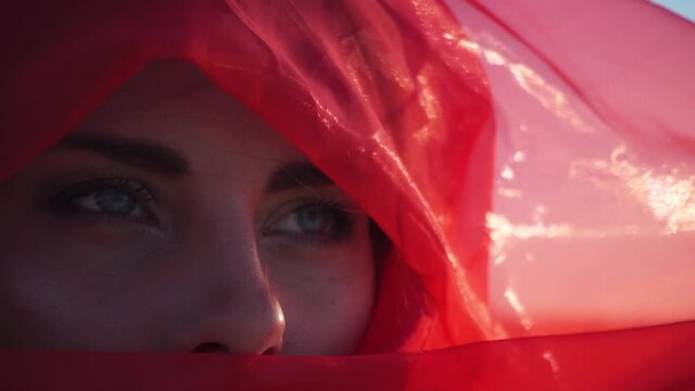 Portrait of beautiful young model woman in burqa yashmak red scarlet transparent shawl, eyes face close macro. Arabic girl concubine. Fashion. Faith limitation, hide your beauty. Abstract slowmotion