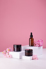 Set of cosmetics containers for cream and essential oil on white podium with fresh spring flowers...