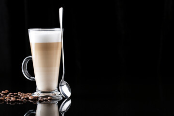coffee with milk, latte macchiato in a glass with a handle and a long spoon on a black background