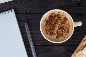 Workplace mockup with a cup of cappuccino coffee on a wooden dark table with a laptop and notepad