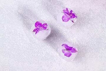 Fototapeta na wymiar Purple flowers frozen in ice cubes on light gray background with copy space