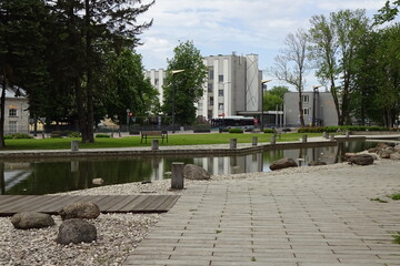 Stone paving walkway in the park on a summer day. Green trees by the water canal. Bus and buildings in the back. Ulemiste, Tallinn, Estonia.