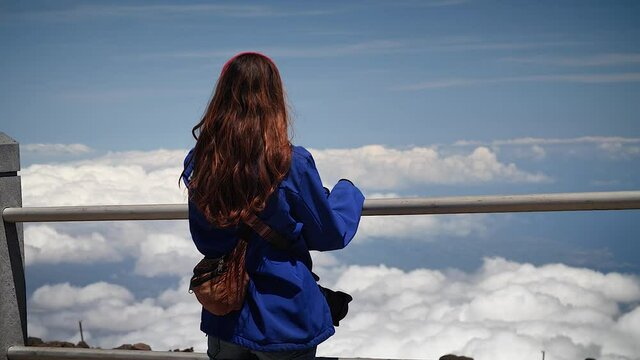 Young woman overlooking clouds above the mountains in Haleakalā National Park, Maui, Hawaii. Mid angle, parallax movement, slow motion, HD.