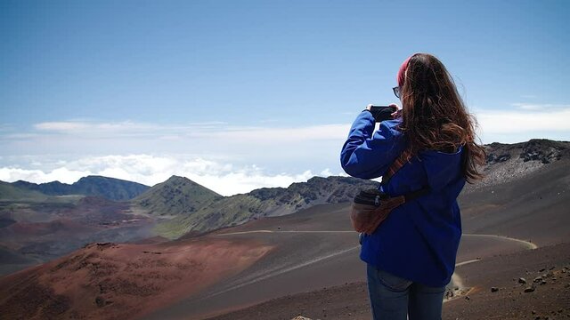 Young woman taking pictures of clouds above the mountains in Haleakalā National Park, Maui, Hawaii. Mid angle, parallax movement, slow motion, HD.