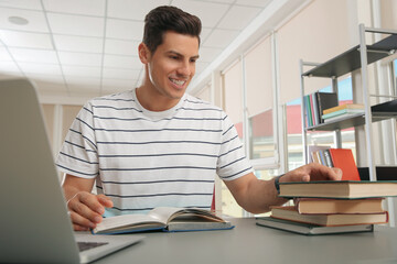 Man with laptop and books studying at table in library