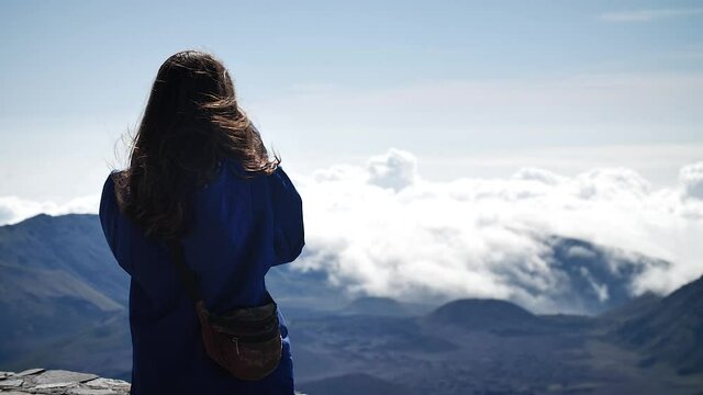 Young woman photographing clouds above the mountains in Haleakalā National Park, Maui, Hawaii. Mid angle, parallax movement, slow motion, HD.