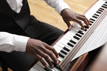 African-American man playing piano indoors, closeup. Talented musician