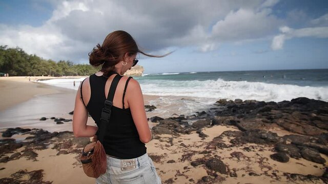 Woman photographing surfers at Shipwreck Beach, Kauai, Hawaii. Mid angle, parallax movement, slow motion, HD.