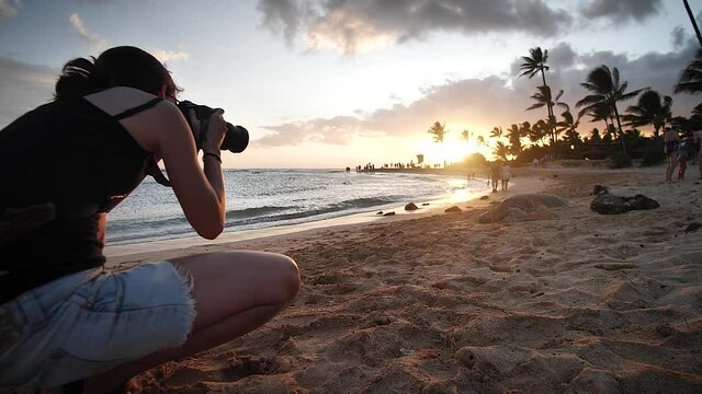 Woman taking a photo on the beach at sunset in Poipu Beach, Kauai, Hawaii. Mid angle, parallax movement, slow motion, HD.