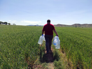 A man walking in the fields, water cans in their hands,