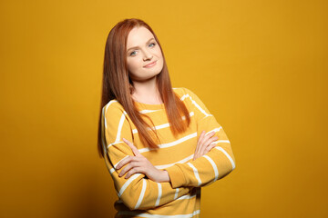 Candid portrait of happy young woman with charming smile and gorgeous red hair on yellow background