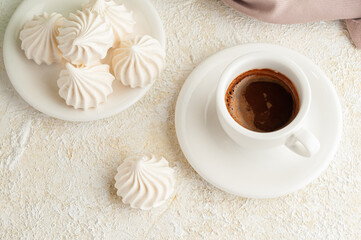 The meringue lies next to a cup of coffee. Next to it is a plate with meringues and a napkin. View from above. Light background.
