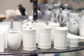White light ceramic bathroom accessories on the counter of the store. Dispensers for liquid soap, glasses for toothbrushes.