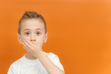 Little preschool boy covered her mouth with her hands. Keep it secret. Space for text. Concept of silence, no talking, I won't say anything. Emotional portrait of kid boy. Yellow background.