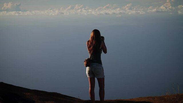 Woman overlooking the ocean from above Na Pali Coast at sunset in Kauai, Hawaii. Mid angle, parallax movement, HD.