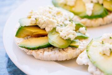Breakfast of puffed wheat toast with avocado and fresh cheese.