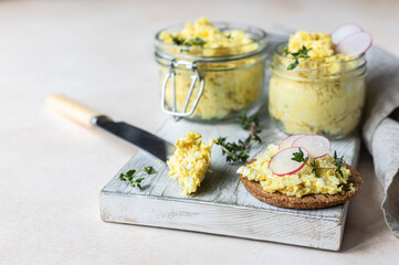 Tartlets with egg pate or salad and radish and thyme on light stone background. Egg dip in glass jar.