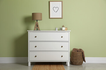Modern white chest of drawers with lamp and decor near light green wall indoors