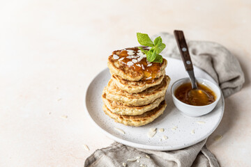 Stack of vegetarian oatmeal pancakes for breakfast decorated with nuts, jam and mint, light stone background.