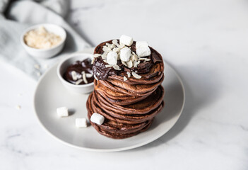 Chocolate pancakes with melted chocolate, ground almond and marshmallow, light background.